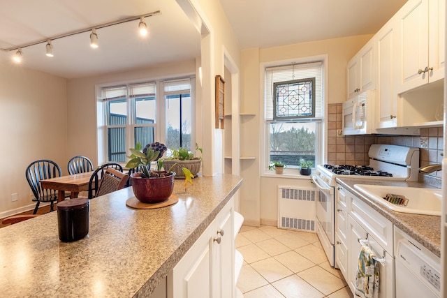 kitchen featuring radiator heating unit, light tile patterned floors, tasteful backsplash, white appliances, and white cabinets