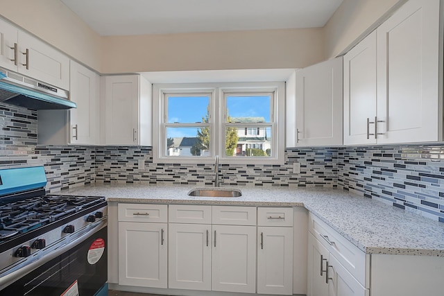 kitchen featuring gas range, white cabinetry, sink, light stone counters, and decorative backsplash