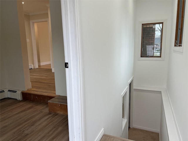 staircase with a baseboard heating unit, crown molding, and hardwood / wood-style floors