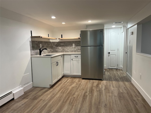 kitchen featuring tasteful backsplash, baseboard heating, stainless steel refrigerator, white cabinets, and sink