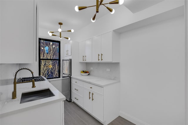 kitchen featuring white cabinetry, sink, light stone countertops, a notable chandelier, and decorative backsplash