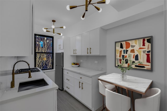 kitchen featuring white cabinets, tasteful backsplash, a notable chandelier, light stone counters, and stainless steel refrigerator