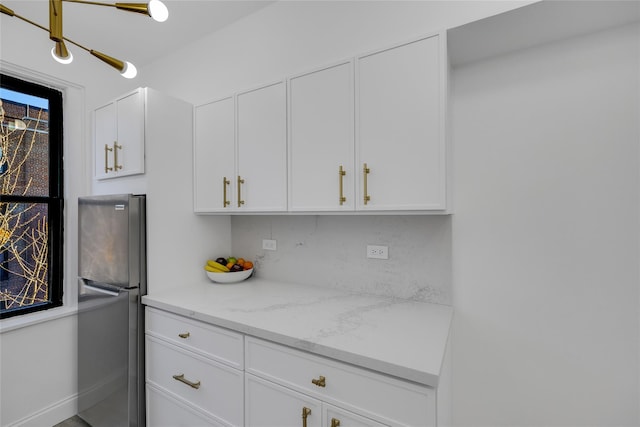 kitchen featuring stainless steel fridge, backsplash, white cabinetry, and light stone counters