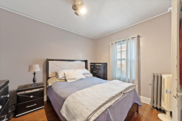 bedroom featuring radiator, dark wood-type flooring, ornamental molding, and a textured ceiling