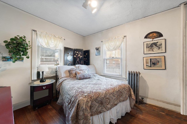 bedroom with radiator, dark wood-type flooring, a textured ceiling, and multiple windows