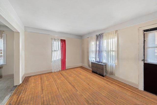 unfurnished room featuring a wealth of natural light, radiator heating unit, and light hardwood / wood-style flooring