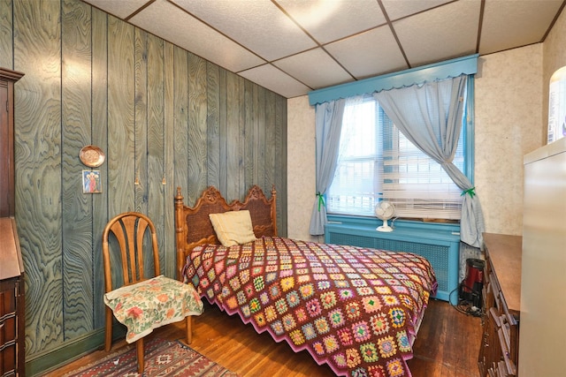 bedroom featuring a paneled ceiling, wooden walls, radiator heating unit, and dark hardwood / wood-style floors