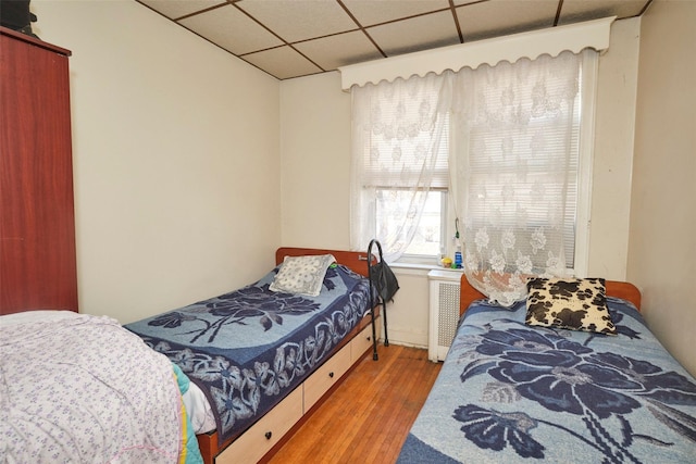 bedroom with hardwood / wood-style flooring, radiator, and a paneled ceiling