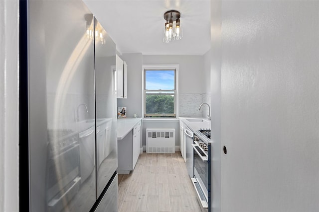 kitchen featuring radiator, sink, light wood-type flooring, appliances with stainless steel finishes, and white cabinetry