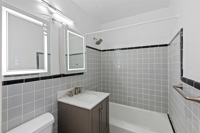 full bathroom with tiled shower / bath, vanity, tile walls, and toilet