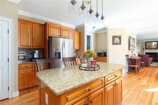 kitchen with pendant lighting, light stone countertops, ornamental molding, a kitchen island, and stainless steel fridge with ice dispenser