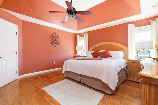 bedroom with a tray ceiling, ceiling fan, and light hardwood / wood-style floors