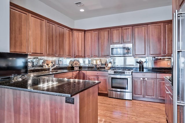 kitchen featuring dark stone counters, sink, light wood-type flooring, appliances with stainless steel finishes, and kitchen peninsula