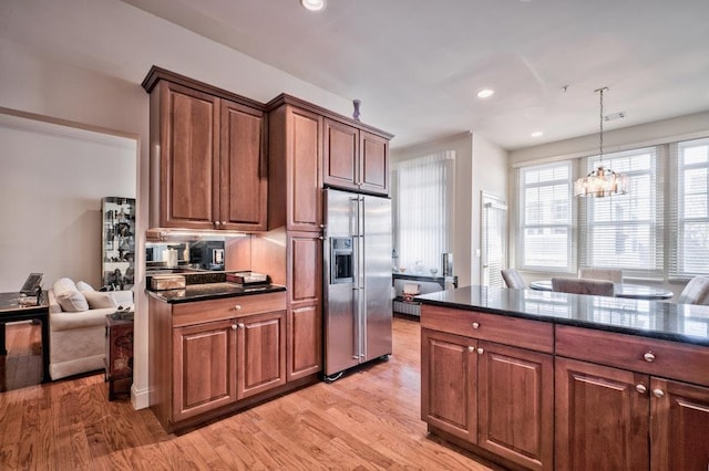 kitchen featuring hanging light fixtures, stainless steel refrigerator with ice dispenser, dark stone countertops, a chandelier, and light wood-type flooring