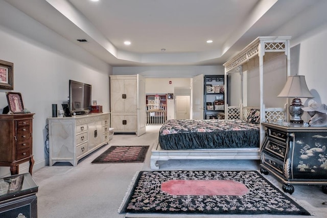 bedroom with light colored carpet and a tray ceiling