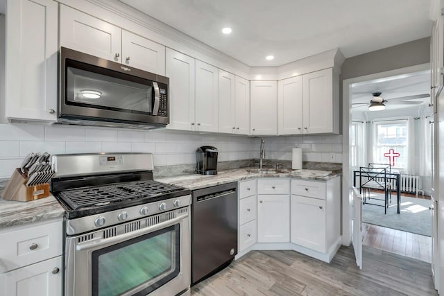 kitchen with white cabinets, sink, appliances with stainless steel finishes, light hardwood / wood-style floors, and light stone counters