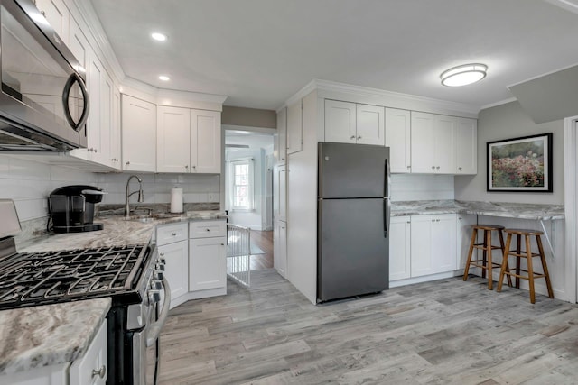 kitchen featuring sink, light stone counters, light hardwood / wood-style floors, white cabinets, and appliances with stainless steel finishes