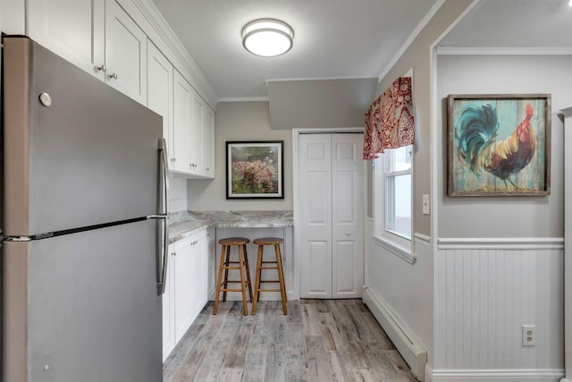 kitchen with stainless steel refrigerator, white cabinetry, light stone counters, a baseboard heating unit, and ornamental molding