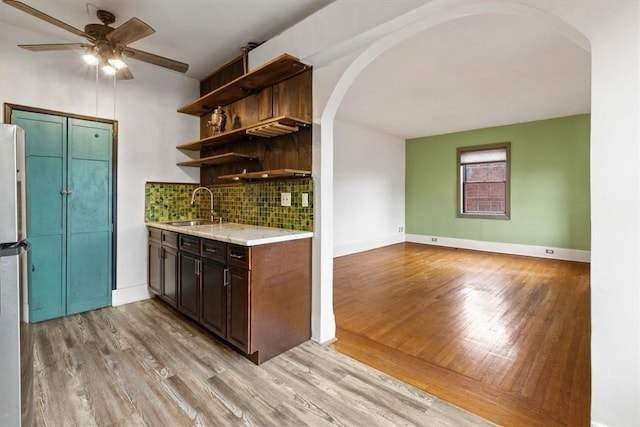 kitchen featuring backsplash, dark brown cabinetry, ceiling fan, sink, and light hardwood / wood-style floors