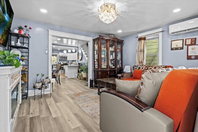 living room featuring an AC wall unit, a fireplace, light hardwood / wood-style floors, and an inviting chandelier