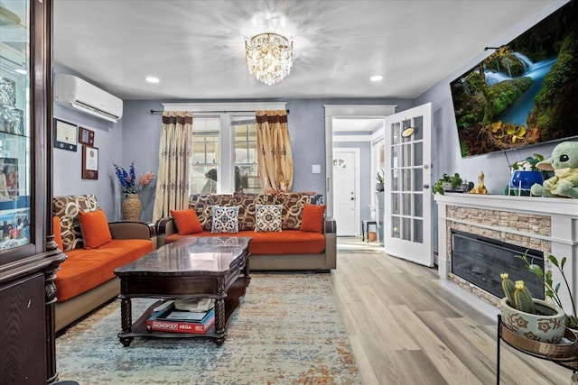 living room featuring a wall mounted AC, a stone fireplace, a notable chandelier, and light wood-type flooring