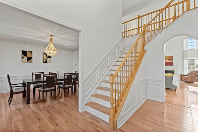 staircase with an inviting chandelier, ornamental molding, and hardwood / wood-style floors