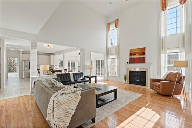 living room with ceiling fan, a towering ceiling, and light hardwood / wood-style floors