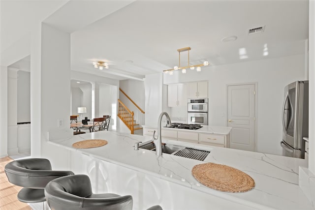 kitchen with pendant lighting, white cabinetry, sink, light stone counters, and stainless steel appliances