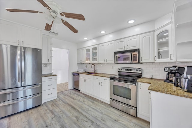 kitchen with white cabinets, sink, light hardwood / wood-style flooring, dark stone countertops, and appliances with stainless steel finishes