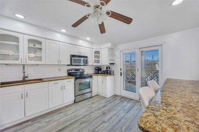 kitchen featuring appliances with stainless steel finishes, backsplash, sink, dark stone countertops, and white cabinetry