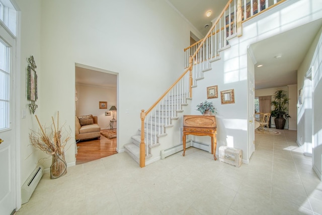 foyer entrance featuring tile patterned flooring, crown molding, baseboard heating, and a high ceiling