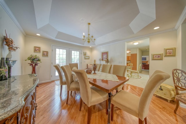 dining space with a raised ceiling, light hardwood / wood-style flooring, an inviting chandelier, and ornamental molding