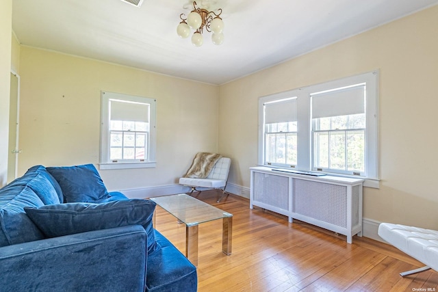 living area featuring wood-type flooring, an inviting chandelier, radiator, and a healthy amount of sunlight