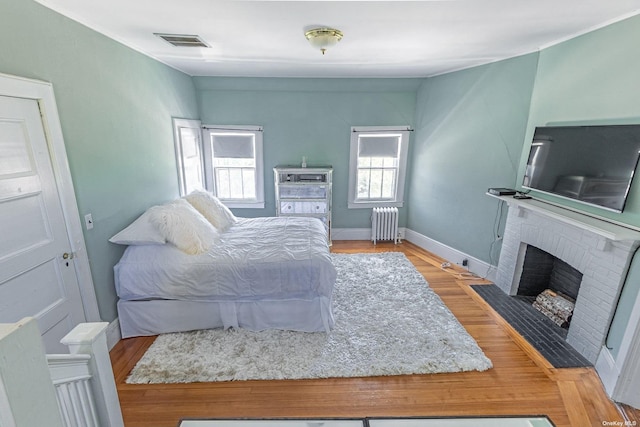 bedroom featuring a fireplace, light hardwood / wood-style floors, and radiator