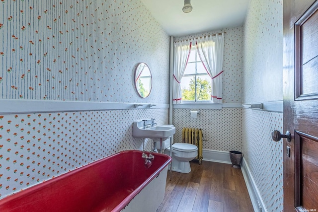 bathroom featuring a tub, radiator, sink, hardwood / wood-style floors, and toilet