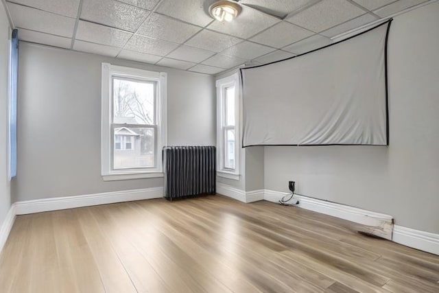 unfurnished room featuring a healthy amount of sunlight, light wood-type flooring, a drop ceiling, and radiator heating unit