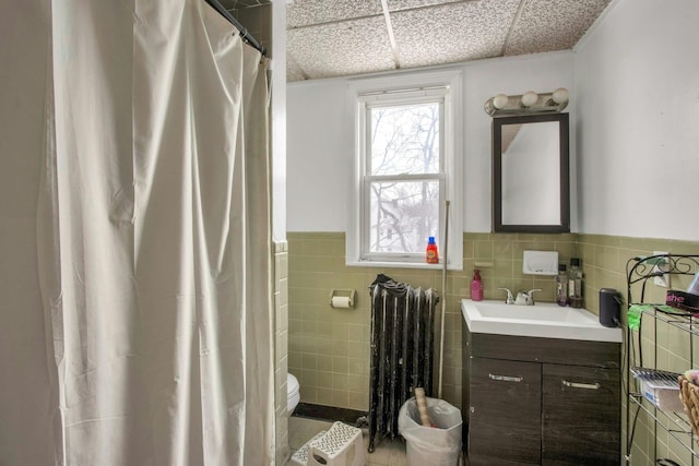 bathroom with radiator heating unit, a paneled ceiling, vanity, tile walls, and toilet