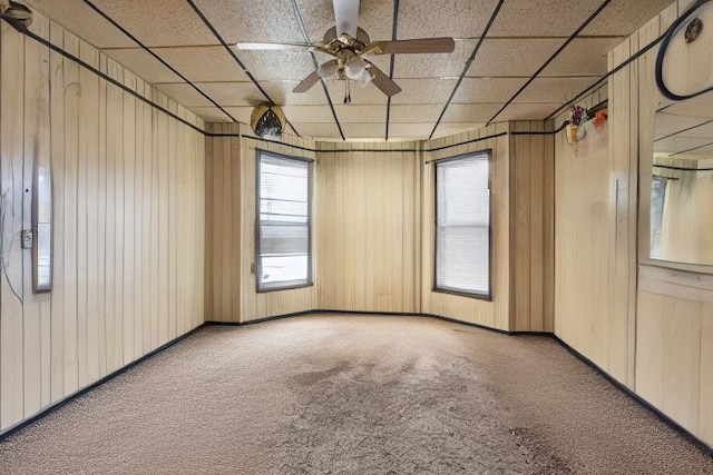 spare room featuring light carpet, ceiling fan, plenty of natural light, and wooden walls