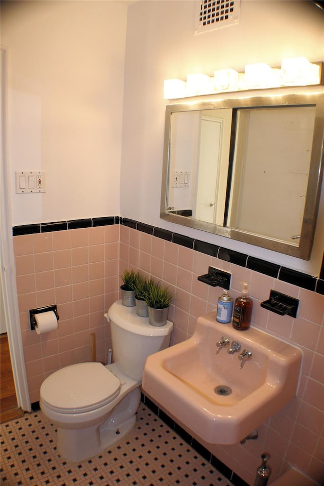 bathroom with toilet, tile patterned flooring, tile walls, and sink