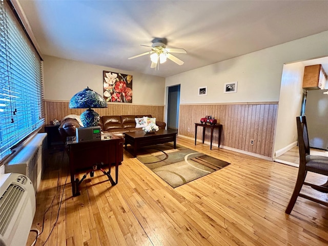 living room with light hardwood / wood-style floors, ceiling fan, and wood walls