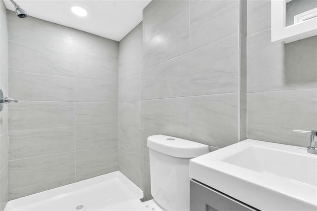 bathroom featuring vanity, toilet, a shower, and tile walls