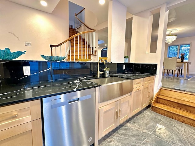 kitchen featuring stainless steel dishwasher, sink, light brown cabinets, a notable chandelier, and dark stone countertops