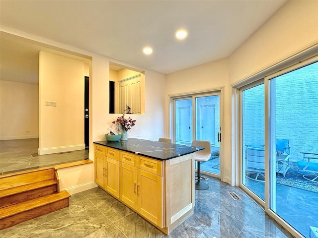 kitchen with kitchen peninsula, light brown cabinets, and dark stone countertops