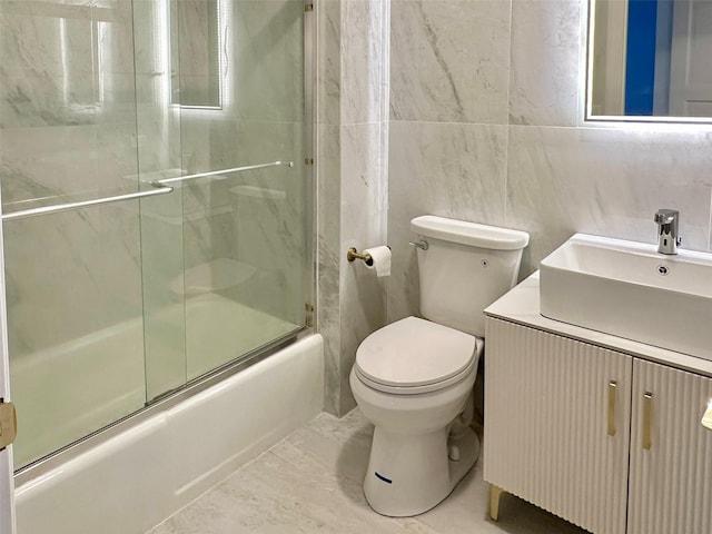 full bathroom with bath / shower combo with glass door, tile walls, vanity, and toilet