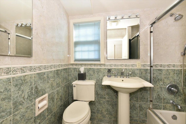 bathroom featuring toilet, bath / shower combo with glass door, and tile walls