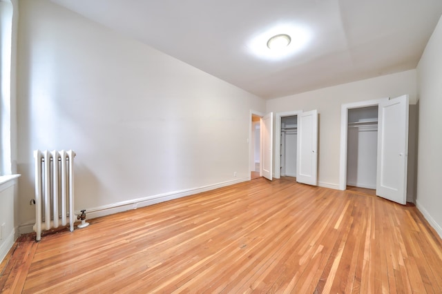 unfurnished bedroom featuring light hardwood / wood-style floors, radiator, and multiple closets