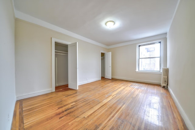 unfurnished bedroom with radiator heating unit, light wood-type flooring, a closet, and ornamental molding