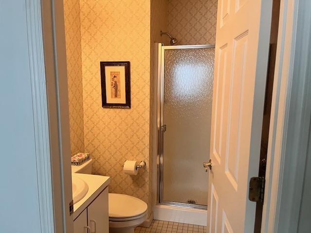 bathroom featuring tile patterned flooring, vanity, a shower with shower door, and toilet