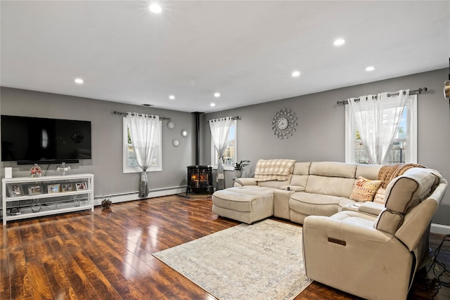 living room featuring baseboard heating, plenty of natural light, a wood stove, and dark hardwood / wood-style floors