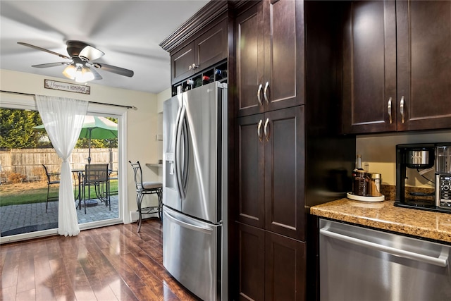 kitchen featuring ceiling fan, dark brown cabinetry, stainless steel appliances, dark hardwood / wood-style flooring, and light stone counters